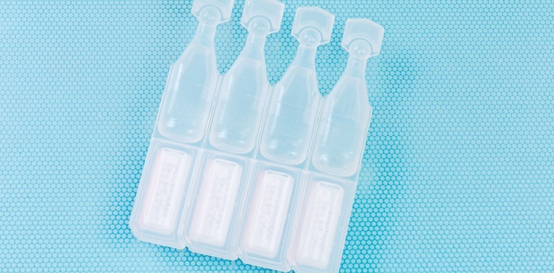 Eye drops in small disposable, plastic ampoules connected in a block on a blue background