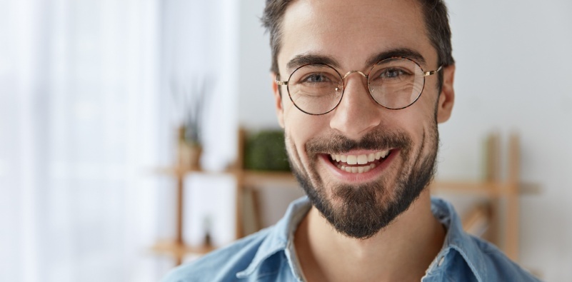 Close up of a middle-aged man wearing round spectacles and smiling at the camera in his home