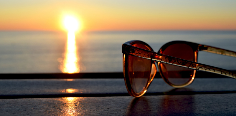 A pair of sunglasses resting on a table overlooking the sea at sunset
