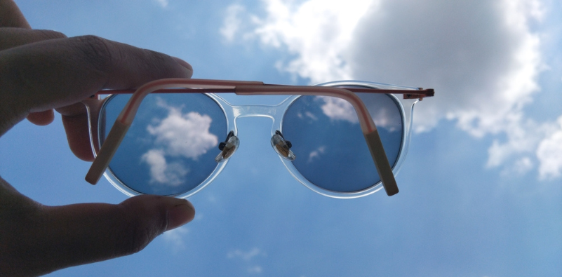 A hand holding a pair of glasses with photochromic lenses against the cloudy sky